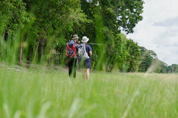 Fototapeta premium Happy tourist hiking walking together over grassland of the plains. Active young adult man trekking through nature grass field over lowland in rural trail. Portrait of real people in peaceful meadow.