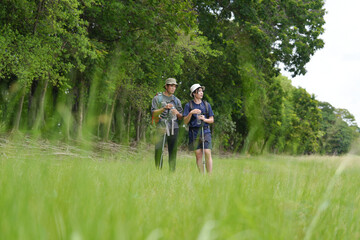Fototapeta premium Happy tourist hiking walking together over grassland of the plains. Active young adult man trekking through nature grass field over lowland in rural trail. Portrait of real people in peaceful meadow.