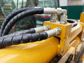 A close-up of robust hydraulic hoses connected to a yellow hydraulic cylinder on heavy machinery,...