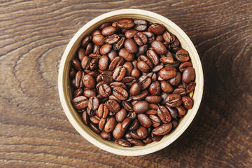Top view of coffee beans. Wooden bowl on rustic table. Brown aromatic roasted grains. Freshly prepared natural caffeine. Morning energy concept. Simple food background with copy space.