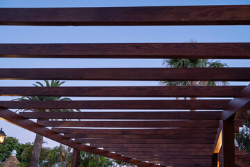 A wooden structure with a roof made of wood. The roof is open, allowing for a view of the sky. The sky is blue and clear, with no clouds visible. The structure is surrounded by palm trees