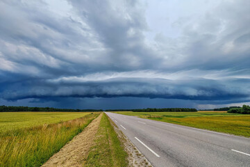 Storm clouds are gathering in a rural landscape with fields above an open road.
