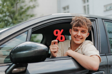 Happy young man sitting inside his car holding red percentage symbol