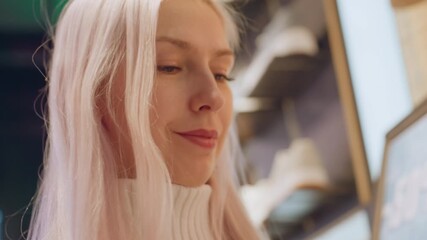 Closeup on poised fashion lover with platinum hair smiling while lifting item inside modern store, eyes glitter under warm spotlights, expressing joy during shopping moment among displays