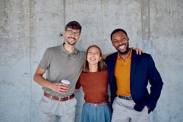 Three cheerful multi-ethnic colleagues in smart casual clothing are smiling with arms around each...