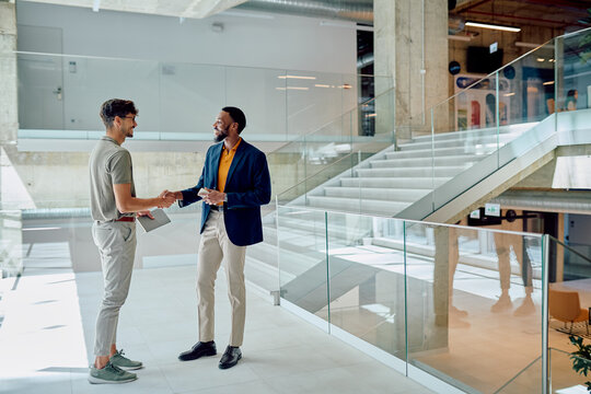 Two businessmen shaking hands in a modern office building lobby, celebrating a successful meeting and solidifying their partnership