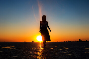 Silhouette of a woman standing on a reflective surface at sunset. Vibrant orange and blue sky....