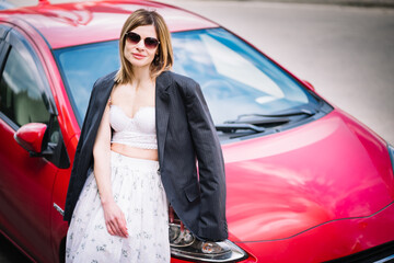 Stylish woman leaning on red car outdoors