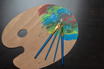 Wooden artist palette with colorful paint and brushes.