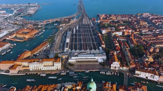 Stunning aerial of Venice's gateway: Santa Lucia train station and bridge. Sunny drone flight over the Grand Canal, showing the city's vibrant connection to mainland Italy.