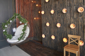 Cozy indoor lounge with hanging chair and string lights on rustic wooden wall design.