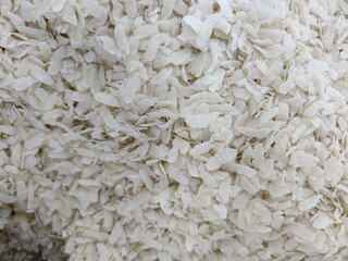 White rice flakes piled high showcasing the texture and size of uncooked cereal grains in a bright light setting