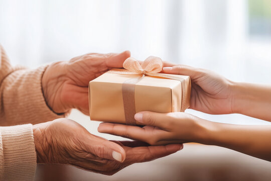 Holiday present exchanging closeup. Bright family photo. Young woman's hands placing a gift box in an older woman's hands. - Powered by Adobe