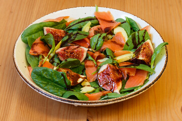 Healthy salad with smoked salmon, spinach, avocado and fig on wooden table