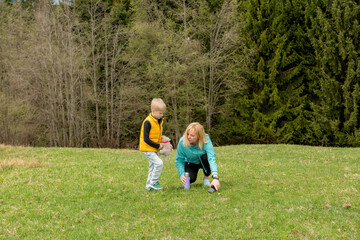 A young grandmother and her grandson explore and observe plants on a green mountain meadow. Family...