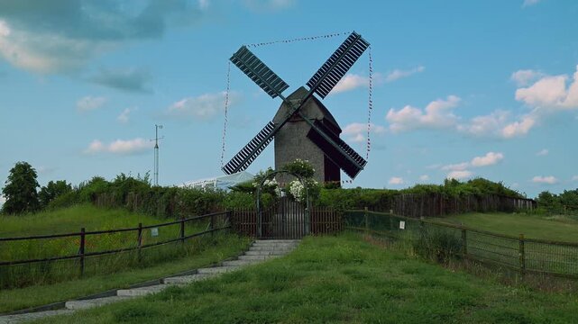 Beautiful german wooden windmill in a serene countryside setting under a bright blue sky, surrounded by lush green fields and pathways, reflecting the beauty of traditional rural architecture.