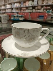 Elegant floral tea cup and saucer displayed in a shop with colorful ceramics in the background during the afternoon