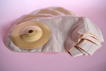 Medical ostomy bags with adhesive rings arranged on pink surface, showcasing hygienic stoma care...