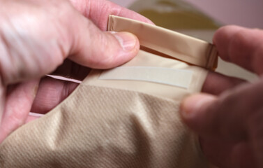 Hands handling the lower draining section of an ostomy bag, showing the secure closure used for...
