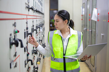 Power engineer in control room operates switches at station while holding laptop, ensuring efficient management and safety of electrical systems with focused attention and care