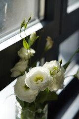 A delicate bouquet of white lisianthus flowers arranged in a clear crystal glass vase. The soft natural lighting and minimalistic background emphasize the beauty and elegance of the blooms.