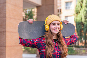 Smiling student girl in braces holding skateboard and wearing yellow headphones and beanie © Renata Hamuda