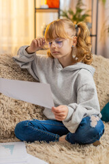 Young teenager girl sits at home, wearing big glasses on face and acting grown-up with slow nods....