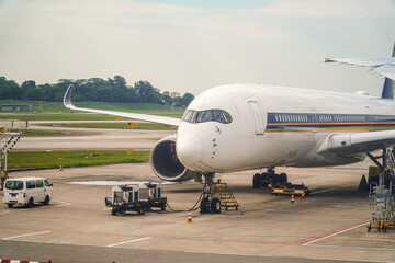 Obraz premium Captured at eye-level, an airplane undergoes maintenance before flight, with equipment alongside. The bright, natural lighting highlights textures and machinery details, creating depth and focus.