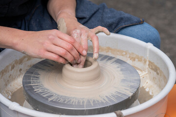 Woman making ceramics in pottery workshop. Close up of female potters hands making bowl. Woman cupped hands around wet clay on a potters wheel. 