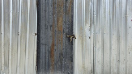 The old silver zinc wall and door have rust stains. The wall covers the part of the house under...