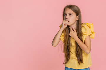 Young child girl touches throat and gently coughs while frowning with a sad face, showing signs of...