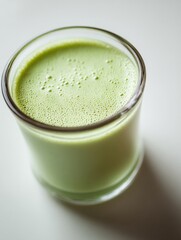 Freshly blended green smoothie in a clear glass with frothy surface, healthy vegetarian beverage, vibrant nutritious drink for wellness