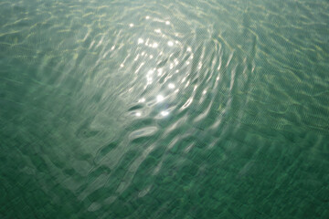 Sunlight reflecting on the surface of water creating a rippling effect in the turquoise liquid
