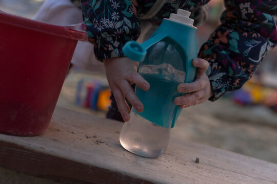 A young child is carefully pouring water into a blue plastic bottle, taking care to avoid spills as they fill it with liquid