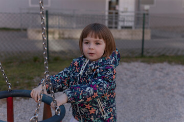 A little girl is happily sitting on a swing at a playground, enjoying her time outdoors while playing and having fun with her friends