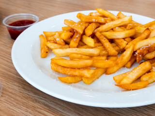 Crispy golden french fries on white plate with ketchup dip on wooden table