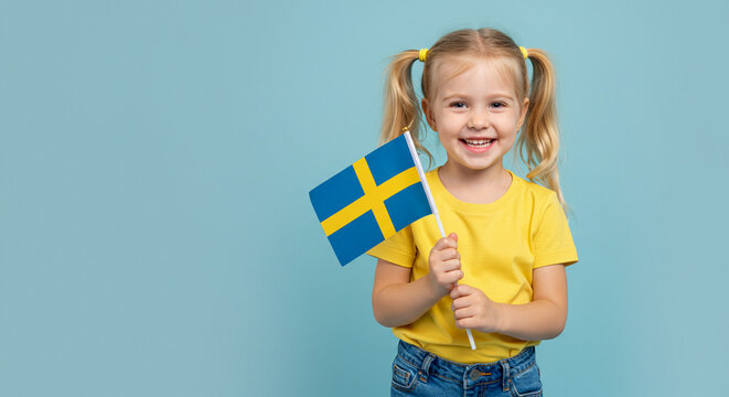 Happy young girl holding Swedish flag and smiling on blue background  