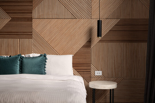 Bed with pillows and geometric timber and wood pattern wall and hanging light. Close up beautiful abstract well interior design luxurious bedroom. Filled with natural light. Wood accent wall.