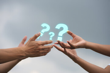 Two hands reaching for floating question marks against a cloudy sky background outdoors