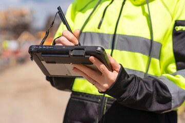 Young woman construction manager uses rugged tablet to record data on construction site