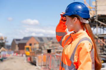 Portrait of young woman construction worker in safety gear standing confidently on building site