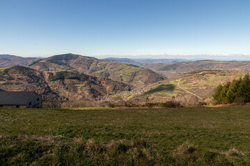 O Cebreiro, Spain. Surrounding valleys and hills near O Cebreiro on a late winter day, with leafless trees and brown tones under a sunny sky with scattered clouds