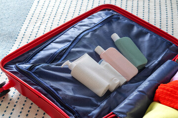 Open suitcase overflowing with clothes and cosmetic tubes on bed in bedroom for a trip. Getting ready for a vacation.