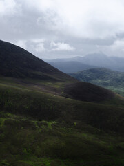 Fototapeta premium Mountains covered in green vegetation recede into the distance. The sky is grey with cloud cover over the scenic landscape of the Coomloughra Horseshoe in County Kerry.