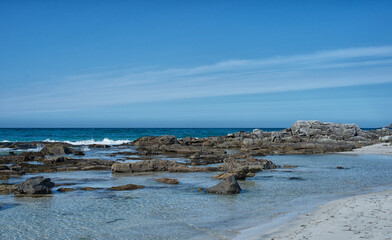 White sand and turquoise blue water.  Small waves of turquoise blue water wash gently across the white sand while mountain peaks rise into the blue sky above.  Typically the words arctic and beach are