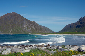 White sand and turquoise blue water.  Small waves of turquoise blue water wash gently across the white sand while mountain peaks rise into the blue sky above.  Typically the words arctic and beach are