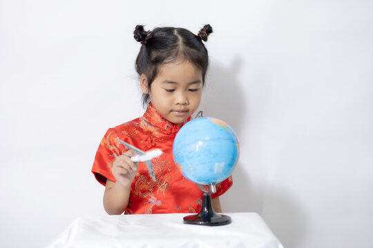Baby girl in Chinese dress holding a toy airplane and a spherical world map on white background. Selective focus at eye and motion blur of hand hold plane.