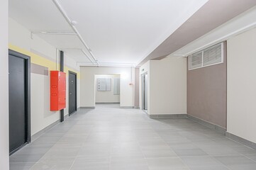 well-lit, modern building corridor with gray tile floors, doors, and a red fire extinguisher box