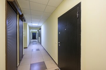 long, well-lit hallway with doors on either side, tiled floor, and a drop ceiling