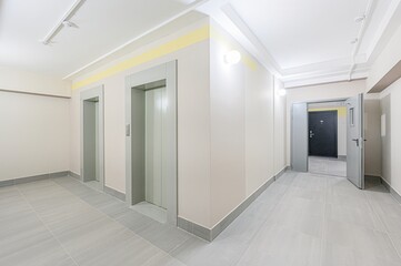 interior shot of a hallway with two elevators on the left and an open doorway to another room on the right. Neutral colors and tile flooring give a clean, modern look